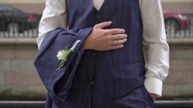 The groom in a vest holds a jacket with a boutonniere in his hands.