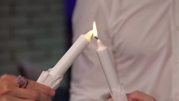 Two people light candle against the other. White traditional candles for holiday — Stockvideo