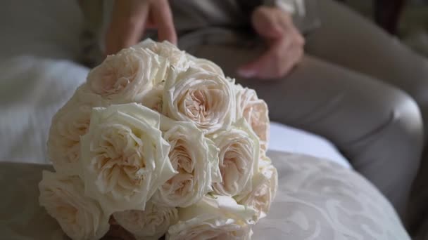 A bride in a gray robe holds a bouquet of white rose flowers in her hands — Vídeo de Stock