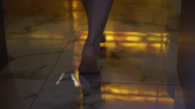 A young woman walks barefoot on the marble tiles on the bathroom floor.