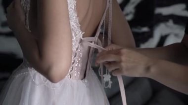 Nedime gelinin gelinliğinin arkasını bağlamasına yardım ediyor..