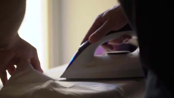 Man ironing a white shirt for a classic suit with an iron on board. — Stockvideo