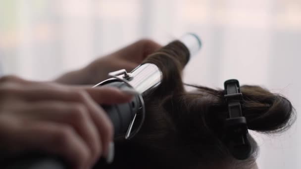Cabeleireiro faz o cabelo das meninas com um ferro de ondulação. Mulher cachos seu cabelo. — Vídeo de Stock