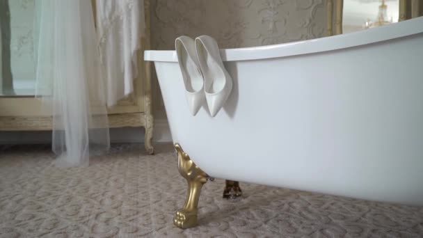 White high heel shoes hang on the bath. Brides dress and long wedding veil. — Stock video