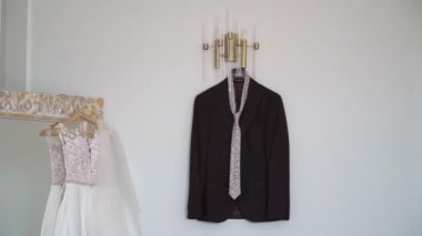 Wedding dress, white bridal gown hanging. Groom suit - black jacket and tie.