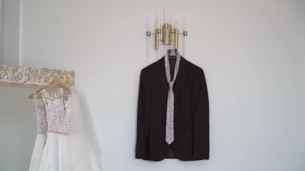 Wedding dress, white bridal gown hanging. Groom suit - black jacket and tie. — Stockvideo