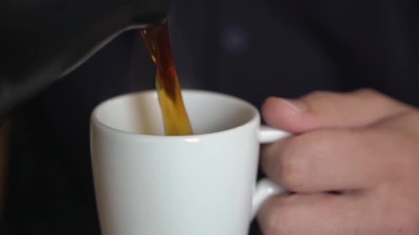 A man pours coffee from a coffee pot or coffee maker into a white cup.
