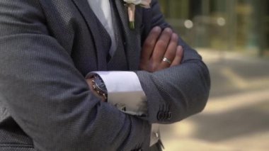 Gri takım elbiseli genç bir adam kollarını kavuşturmuş duruyor. İş adamı ya da damat.