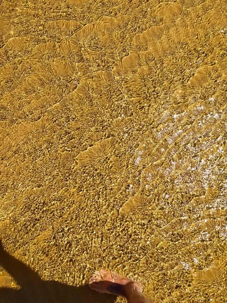 Bright ripples on the surface of the water.Golden sand beneath the brilliant ripples on the surface of the water. Shallow water beach surface, blurred abstract background.