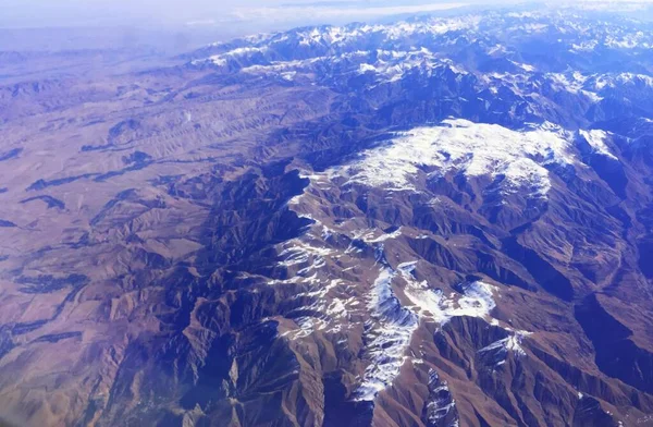Snow-capped mountain peaks of the ridge. Northern snowy mountains. top view from the airplane window. Mountain landscape with snow-capped mountain peaks. Emerald mountain lakes and steep mountain — Stock Photo, Image