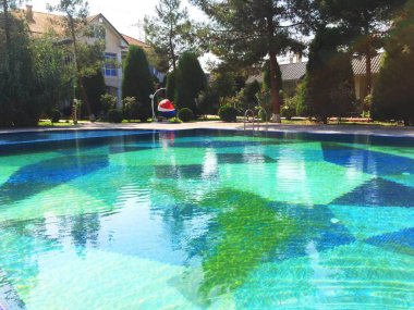 Havuzlu ve güneşli bir otel. Temiz mavi havuz suyu, anlaşıldı. Yakınlarda yeşil ağaçlar ve parlak çiçekler var. Güneşli bir sabahta berrak dağ suyuyla dolu bir havuz. Sonsuz bir havuz.