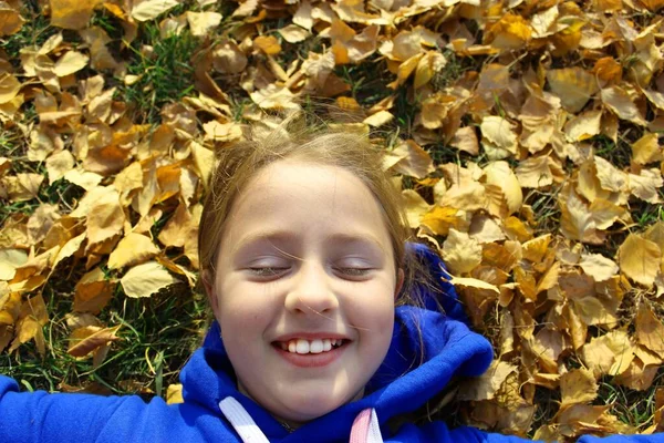 Вид зверху портрет щасливої дитини розважається на відкритому повітрі в осінньому парку. Усміхнений дитина лежить на зеленій траві на жовтому тлі розмитого листя. Високоякісна дівчинка, мила маленька дівчинка — стокове фото