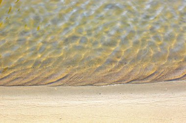 Yakın çekim ve parlak şeffaf sarı kum ve kumsaldaki temiz suyla taşların üst görüntüsü. Açık deniz, yazın güneşin altında doğal bir dinlenme yerinin güzelliğini gözler önüne serer. Bir...