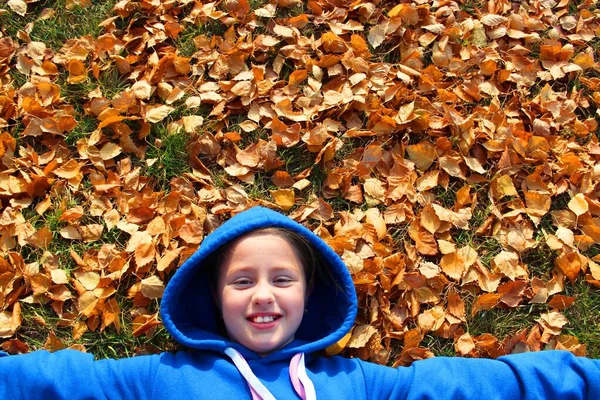 가을 공원의 야외에서 재미있게 노는 행복 한 아이의 맨 위 사진. 푸른 잔디 위에 누르스름 한 배경에 누워 미소짓는아이. 밝고 행복 한 어린 소녀, 귀여운 소녀 — 스톡 사진