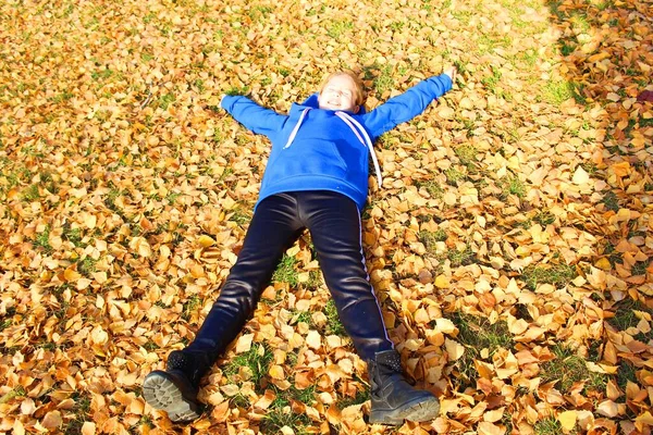 Top view portret van gelukkig kind plezier hebben buiten in het najaar park. Glimlachend kind liggend op groen gras tegen gele bladeren wazig achtergrond. Hoge kwaliteit fotogelukkig klein meisje, schattig klein meisje — Stockfoto