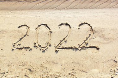 Yeni yıl 2022. Mesaj kumlu bir plajın arka planında yazılmış. 2022 yılının merhaba konsepti. Yeni yıl Noel 'i. metin için kopyalama alanı ile. Parlak görünümün üst ve yakın görüntüsü