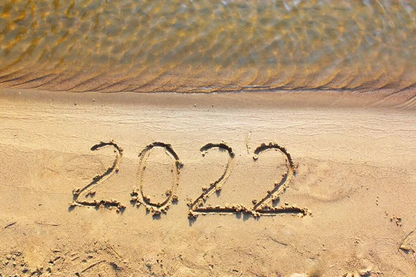 New Year 2022. Message written on the background of a sandy beach. hello concept for the upcoming new year 2022. New Year Christmas. with copy space for text. Close-up and top view of shiny — Stock Photo, Image