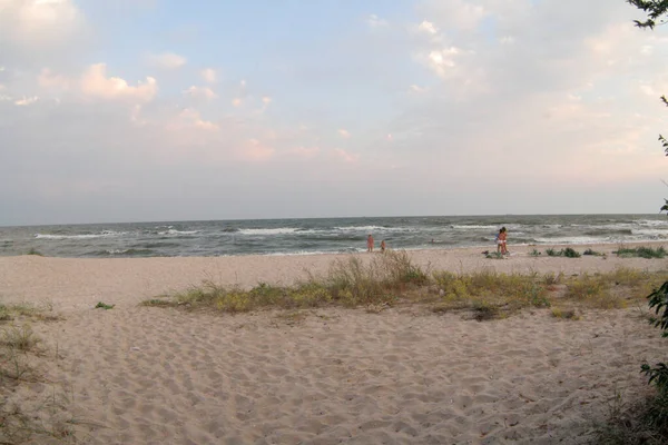 Tengerpart gyerekekkel a homokos strandon a nap napján. A homokos part hullámai sodródnak. A nap égboltja felhőkkel. Tengerparti háttér egy poszt, képernyővédő, tapéta, képeslap, poszter, banner, borító — Stock Fotó