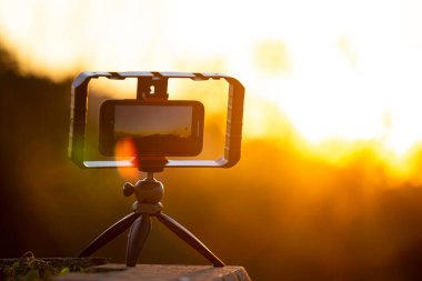 Gün batımının arka planındaki tripodun üzerindeki kamera..