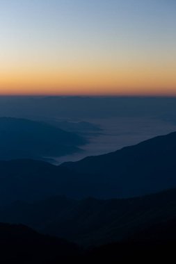 Sabahın ilk ışıklarıyla gökyüzünün görünüşü ve üst üste binen dağlar.