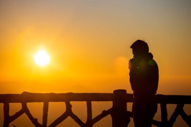 Gün batımı ve gün ışığı sisi olan siluet fotoğrafçı.