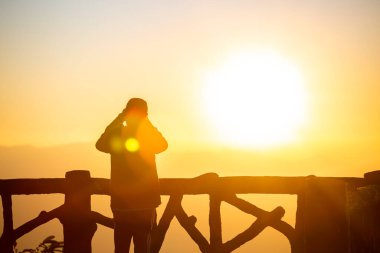 Gün batımı ve gün ışığı sisi olan siluet fotoğrafçı.