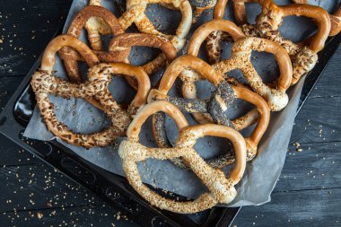 Taze ev yapımı yumuşak krakerler. Siyah arka planda tohumları olan farklı pişmiş simit türleri..