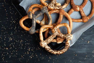 Taze ev yapımı yumuşak krakerler. Siyah arka planda tohumları olan farklı pişmiş simit türleri..