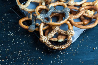 Taze ev yapımı yumuşak krakerler. Siyah arka planda tohumları olan farklı pişmiş simit türleri..