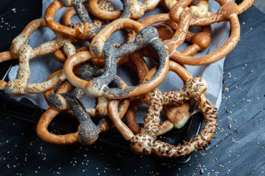 Taze ev yapımı yumuşak krakerler. Siyah arka planda tohumları olan farklı pişmiş simit türleri..