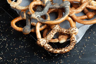 Taze ev yapımı yumuşak krakerler. Siyah arka planda tohumları olan farklı pişmiş simit türleri..