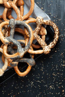 Taze ev yapımı yumuşak krakerler. Siyah arka planda tohumları olan farklı pişmiş simit türleri..