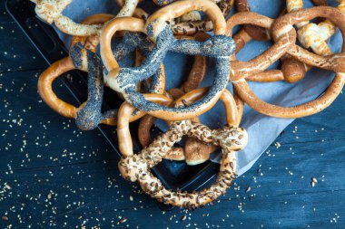 Taze ev yapımı yumuşak krakerler. Siyah arka planda tohumları olan farklı pişmiş simit türleri..