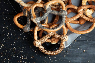 Taze ev yapımı yumuşak krakerler. Siyah arka planda tohumları olan farklı pişmiş simit türleri..