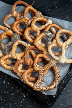 Taze ev yapımı yumuşak krakerler. Siyah arka planda tohumları olan farklı pişmiş simit türleri..