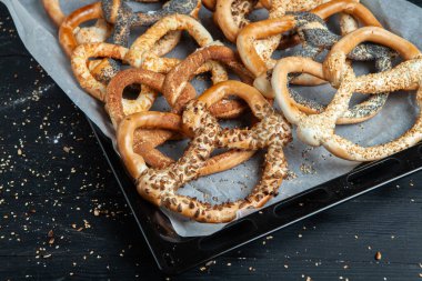 Taze ev yapımı yumuşak krakerler. Siyah arka planda tohumları olan farklı pişmiş simit türleri..