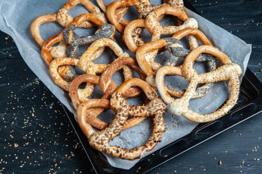 Taze ev yapımı yumuşak krakerler. Siyah arka planda tohumları olan farklı pişmiş simit türleri..