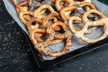 Taze ev yapımı yumuşak krakerler. Siyah arka planda tohumları olan farklı pişmiş simit türleri..