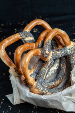 Taze ev yapımı yumuşak krakerler. Siyah arka planda tohumları olan farklı pişmiş simit türleri.