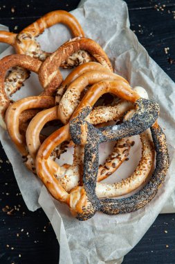 Taze ev yapımı yumuşak krakerler. Siyah arka planda tohumları olan farklı pişmiş simit türleri.