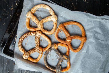 Taze ev yapımı yumuşak krakerler. Siyah arka planda tohumları olan farklı pişmiş simit türleri.