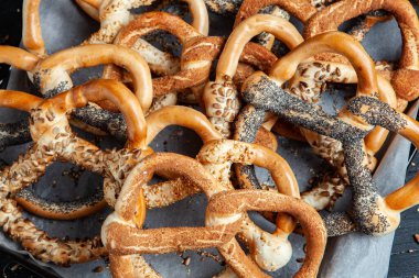 Taze ev yapımı yumuşak krakerler. Siyah arka planda tohumları olan farklı pişmiş simit türleri.