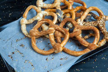 Taze ev yapımı yumuşak krakerler. Siyah arka planda tohumları olan farklı pişmiş simit türleri.
