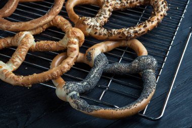 Taze ev yapımı yumuşak krakerler. Siyah arka planda tohumları olan farklı pişmiş simit türleri..