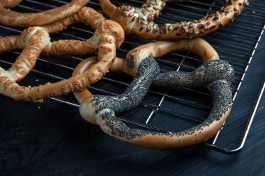 Taze ev yapımı yumuşak krakerler. Siyah arka planda tohumları olan farklı pişmiş simit türleri..