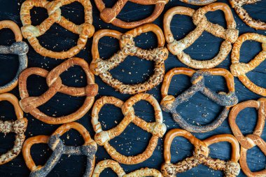 Taze ev yapımı yumuşak krakerler. Siyah arka planda tohumları olan farklı pişmiş simit türleri..