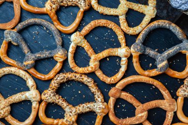 Taze ev yapımı yumuşak krakerler. Siyah arka planda tohumları olan farklı pişmiş simit türleri..