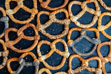 Taze ev yapımı yumuşak krakerler. Siyah arka planda tohumları olan farklı pişmiş simit türleri..
