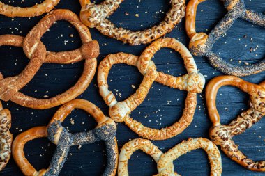 Taze ev yapımı yumuşak krakerler. Siyah arka planda tohumları olan farklı pişmiş simit türleri..