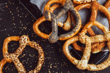 Taze ev yapımı yumuşak krakerler. Siyah arka planda tohumları olan farklı pişmiş simit türleri..
